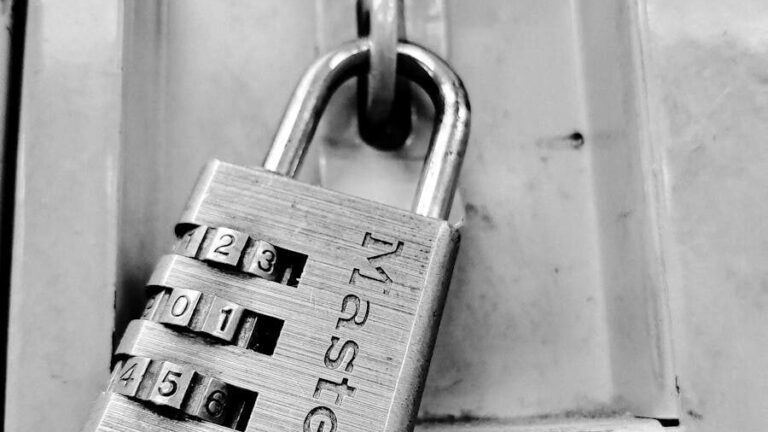Black and white close-up of a combination padlock on a secure metal locker, symbolizing protection.